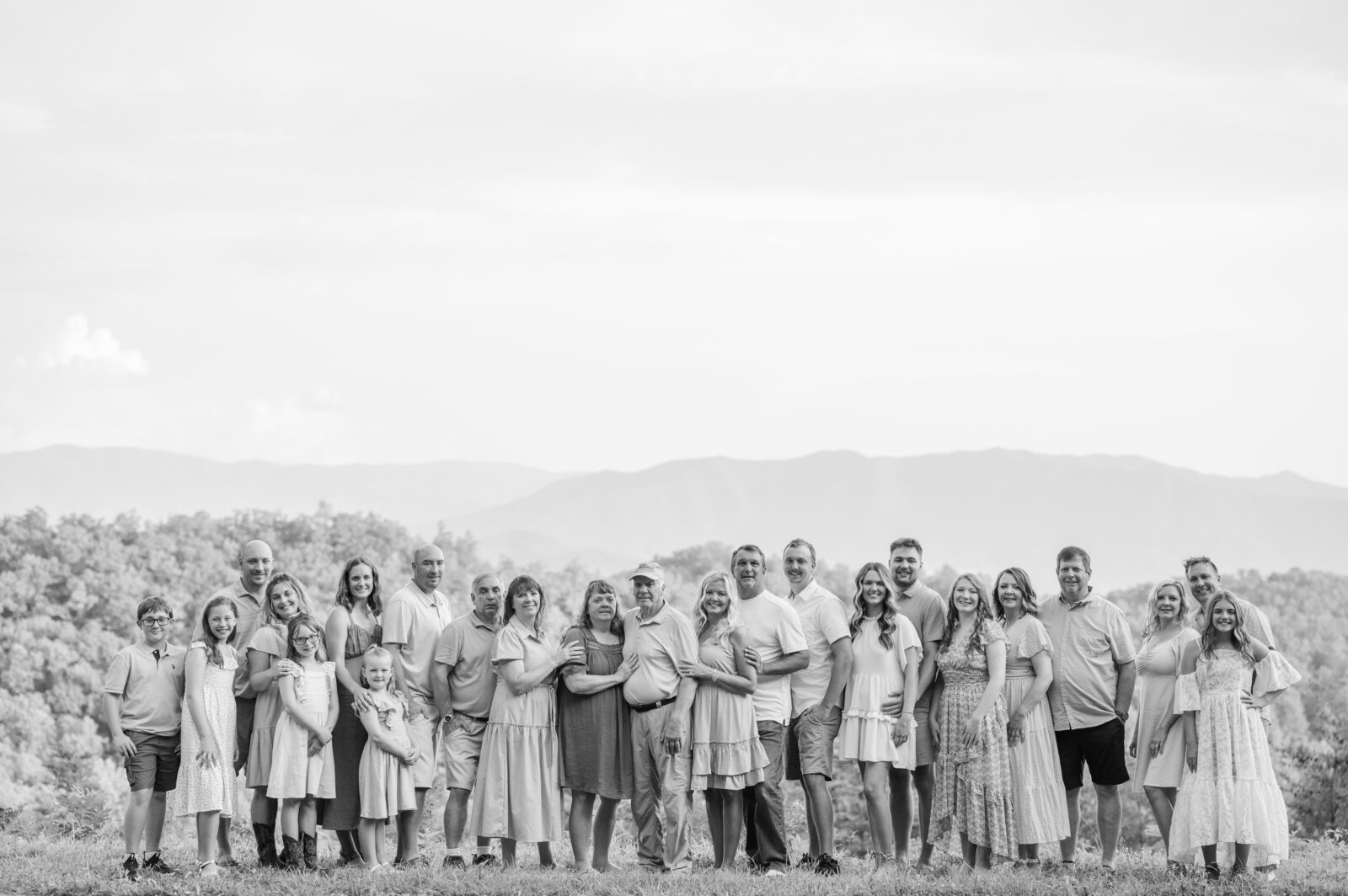 black and white family portrait session in Gatlinburg with a large extended family cuddles up smiling for the camera as a Gatlinburg photographer takes their photo