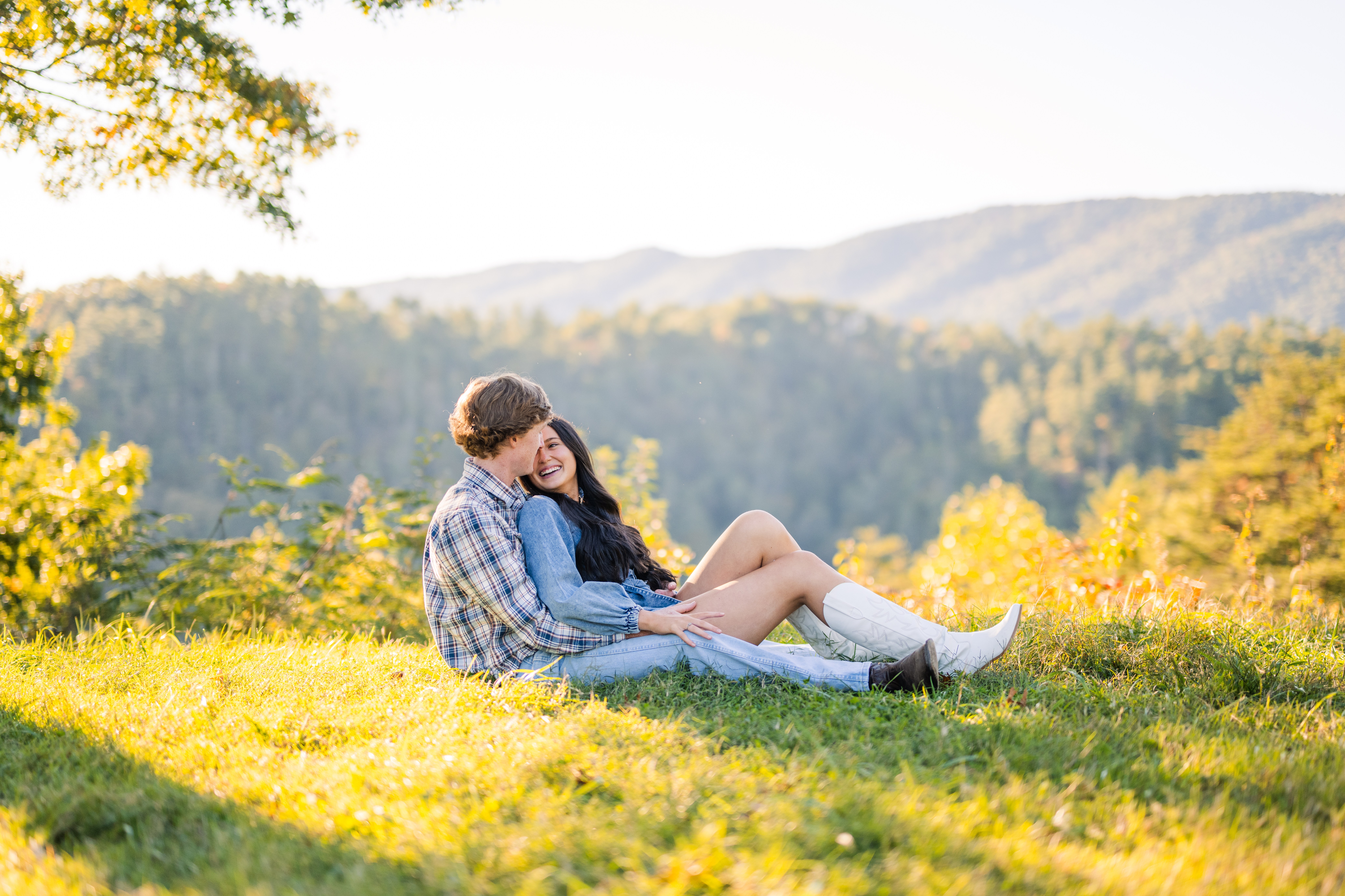 Engagement session in Great Smoky Mountains National Park with couple cuddling at sunset and layered mountains in the background.