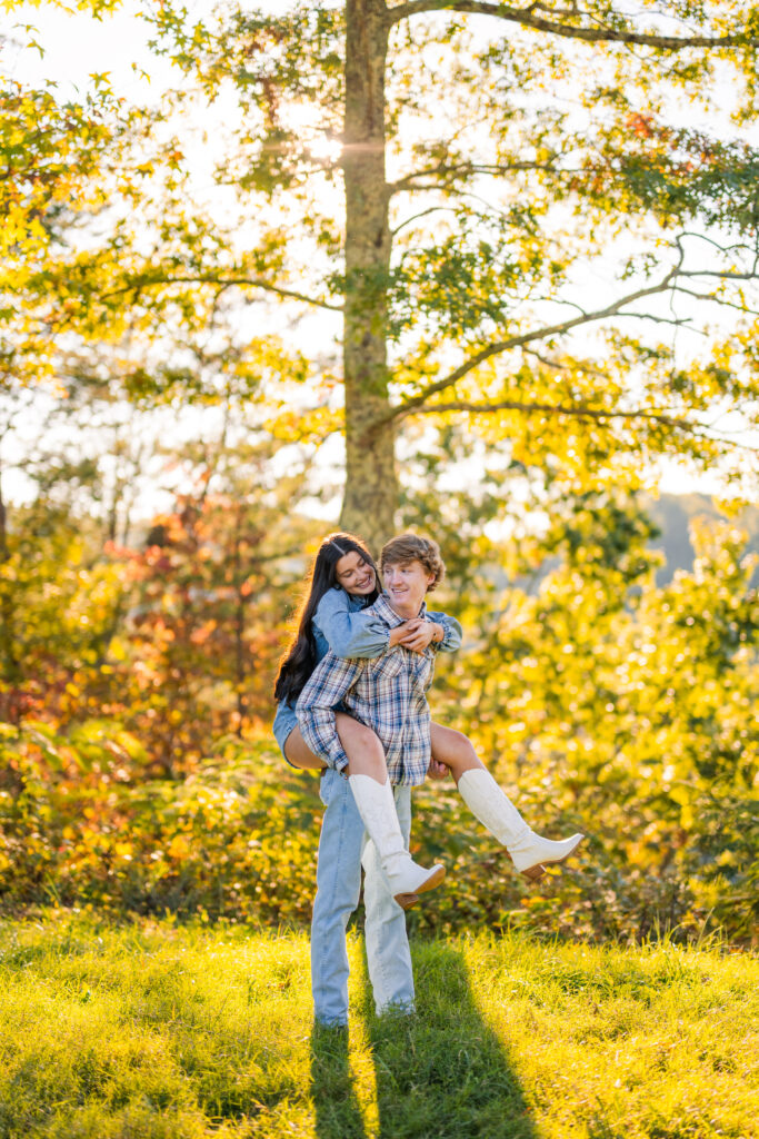 Man giving woman a piggyback ride at sunset with golden glow and fall colors during engagement session on vacation in Pigeon Forge, Tennessee.