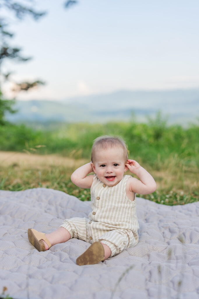 a smiling baby sitting on a blanket in the great smoky mountains national park in gatlinburg, tennessee