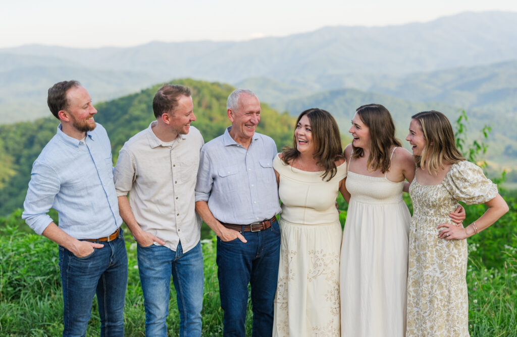 An older mom and dad surrounded by all of their adult children hugging and laughing while having their portraits taken by a photographer on vacation in Gatlinburg, Tennessee