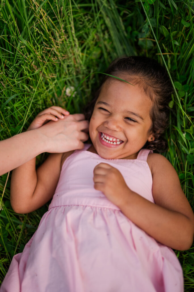 a young girl laying in the thick grass in the great smoky mountains national park laughing as her mom tickles her