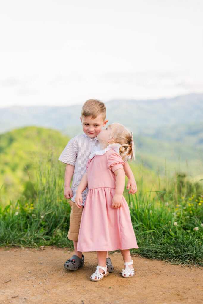 Gatlinburg family photographer captures young girl kissing her older brother on the cheek with surprised reaction during Smoky Mountain vacation.