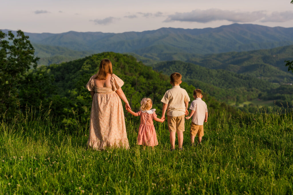 A mom and her three kids all holding hands looking off at the beautiful mountains in Gatlinburg, Tennessee