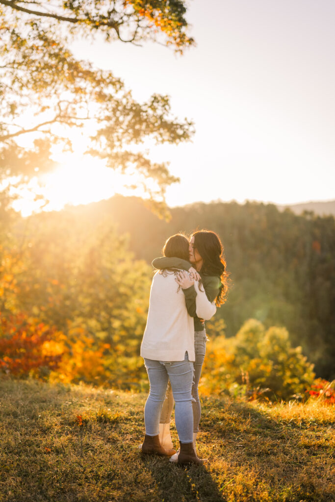 Lesbian couple hugging during intimate moment at sunset with golden glow, fall leaves, and mountains during Gatlinburg engagement session in Tennessee.