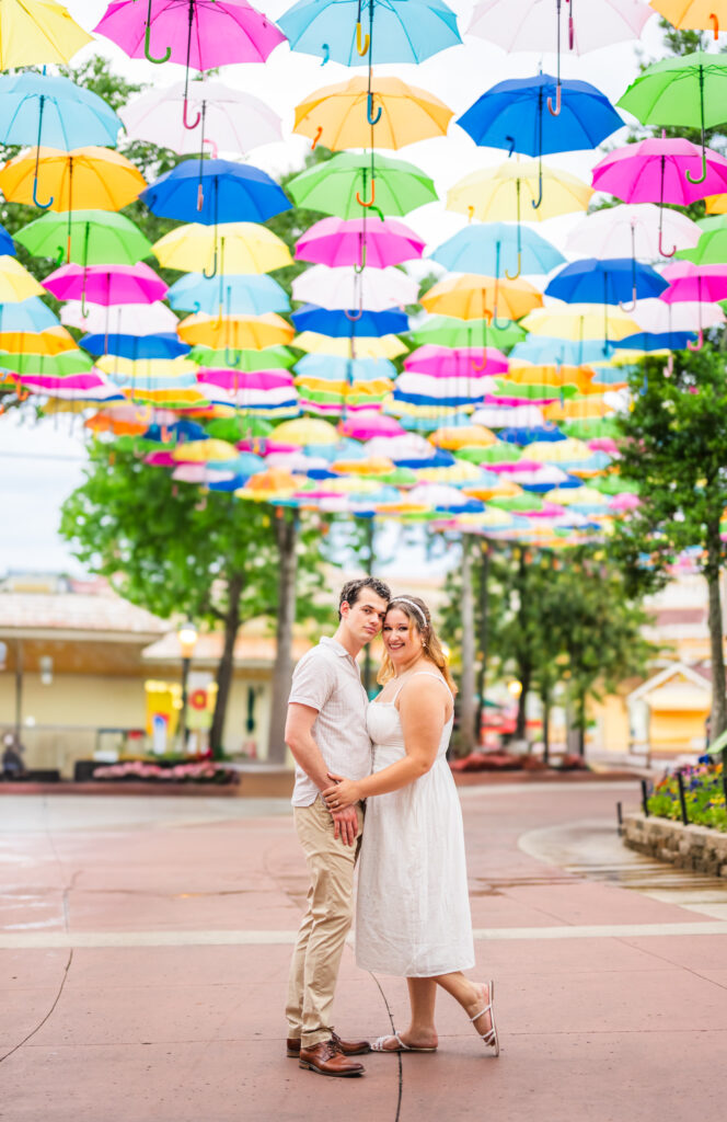 Engaged couple cuddling and smiling under colorful umbrellas at Dollywood during engagement session in Pigeon Forge, Tennessee.