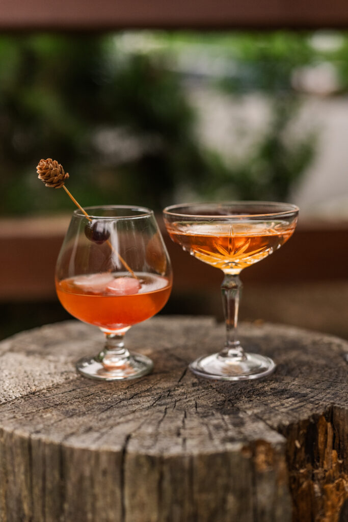 Two craft cocktails sitting on a wooden stump by the outdoor fireplace at The Greenbrier Restaurant bar in Gatlinburg, Tennessee, in the Smoky Mountains.