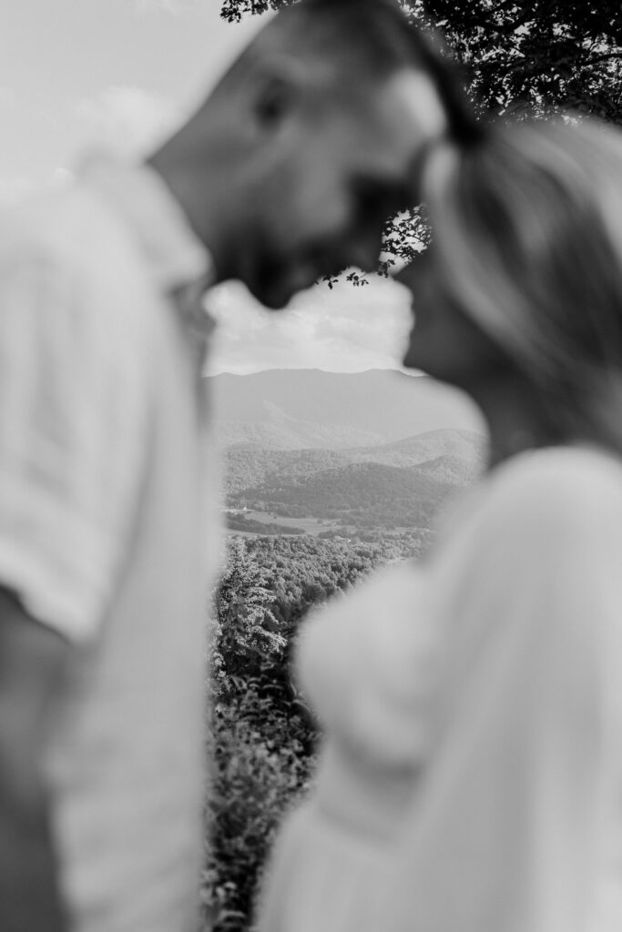 Engaged couple touching foreheads in foreground with mountains in the distance during Smoky Mountains engagement session
