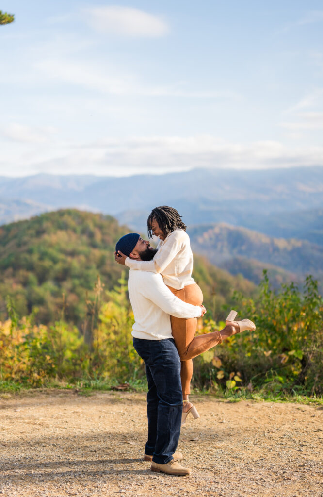 Gatlinburg engagement photographer captures Black couple embracing with vibrant fall mountains in the background during Smoky Mountains session.