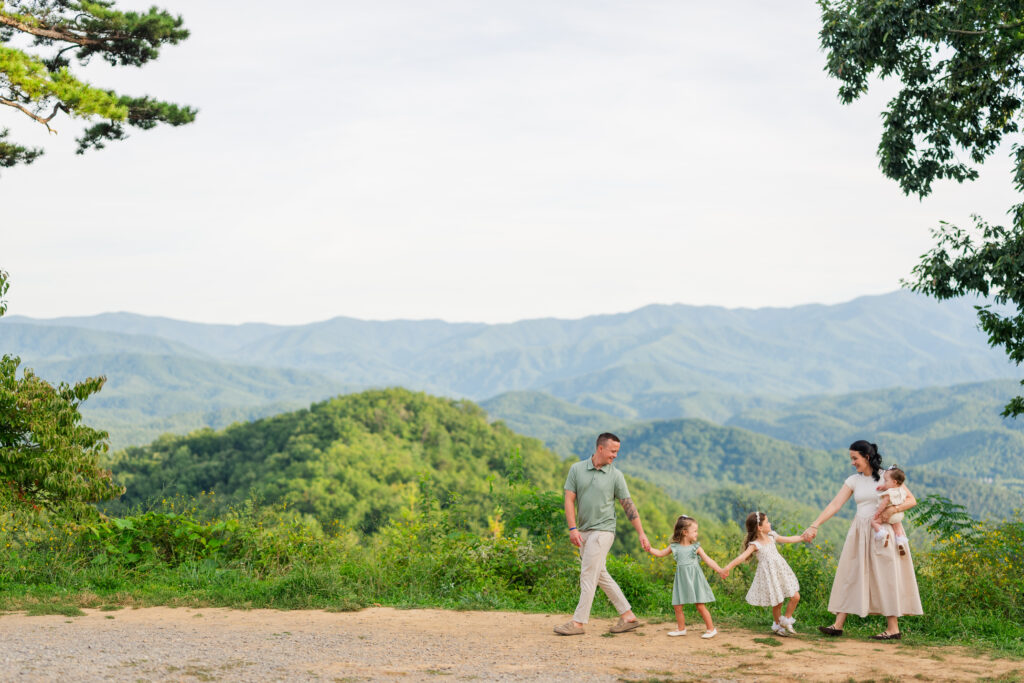Smoky Mountain photographer captures family portraits in the mountains while a dad leads his family along a path as they are all smiling at each other laughing.