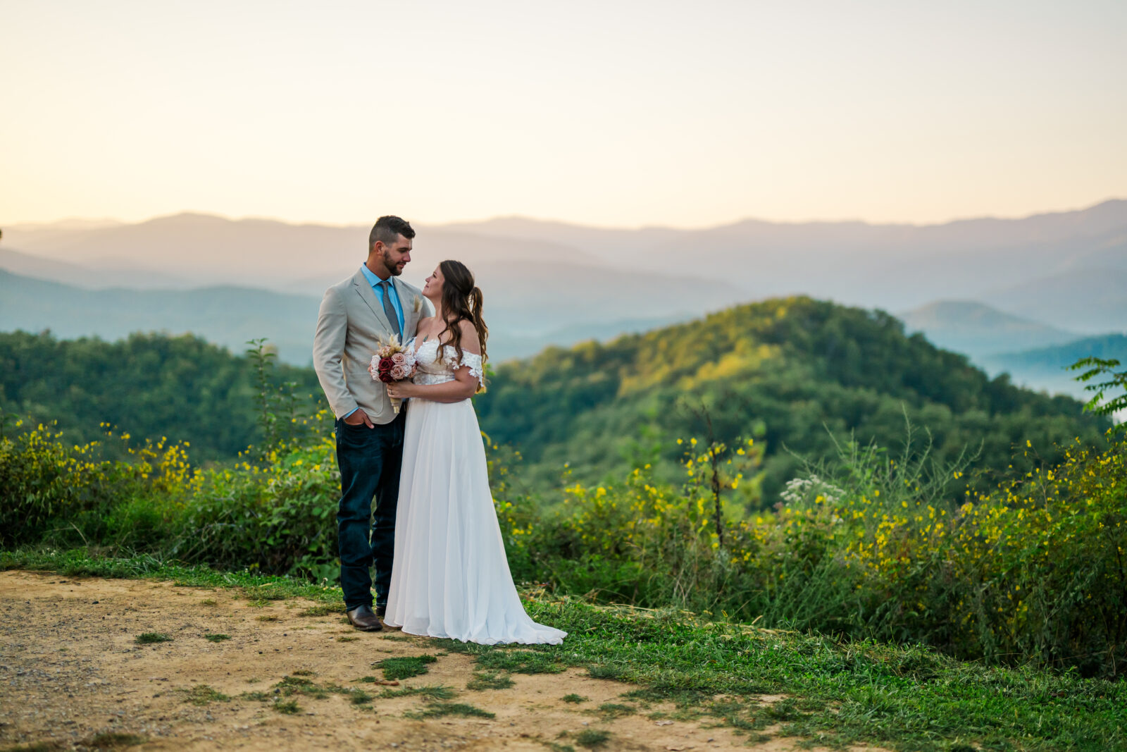 Couple exchanging a loving gaze as the sun rises over the Smoky Mountains, casting pink and orange hues across the ridges during their Gatlinburg elopement.