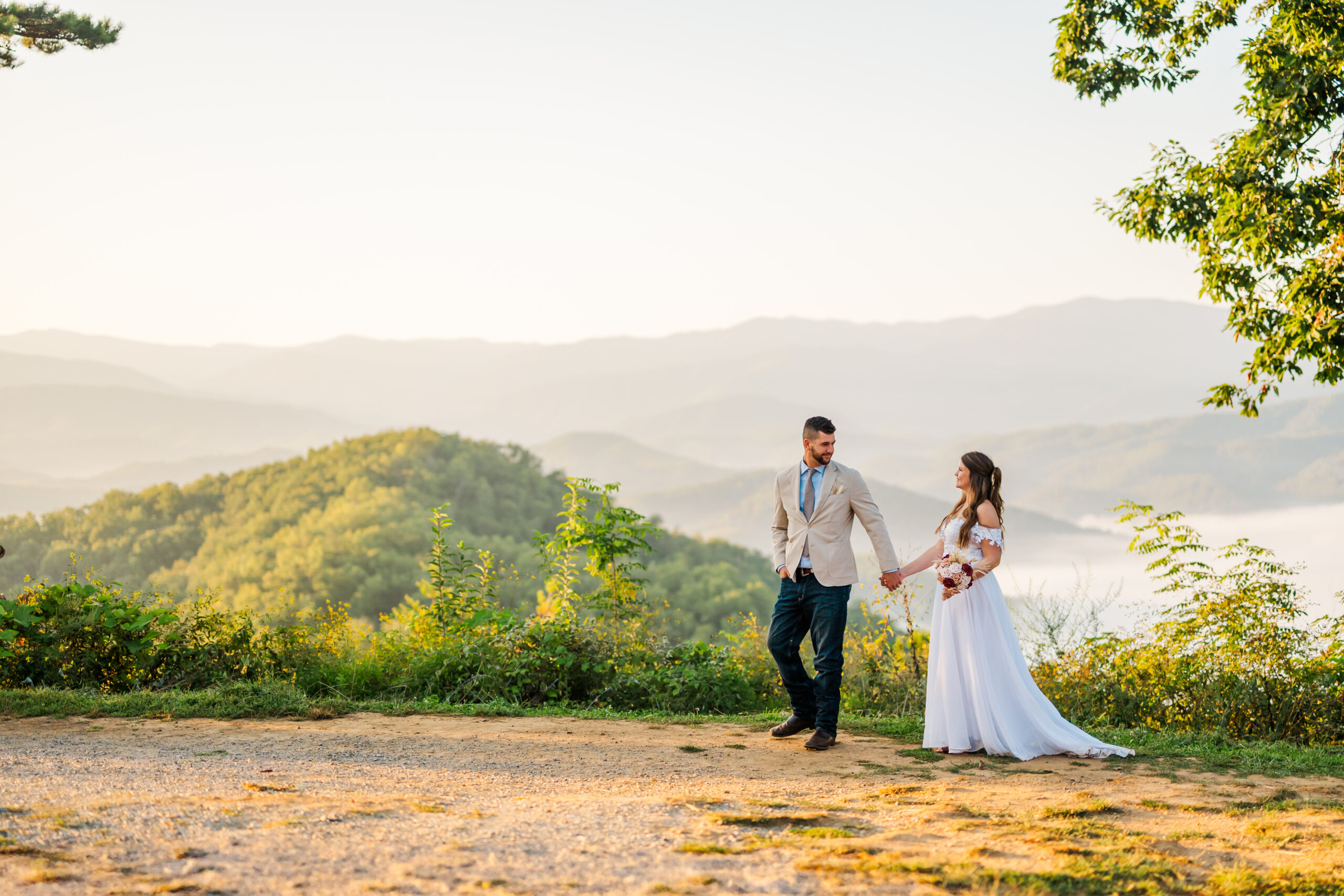 Groom leading his bride across a mountain overlook at sunrise with the Smoky Mountains in the background — romantic Gatlinburg sunrise elopement photography.