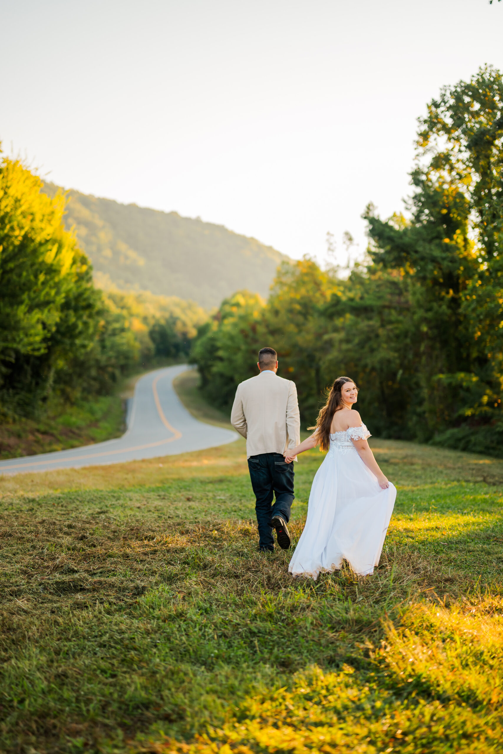 Bride and groom holding hands and running toward the sunrise in the Smoky Mountains, smiling joyfully during their Gatlinburg elopement session.