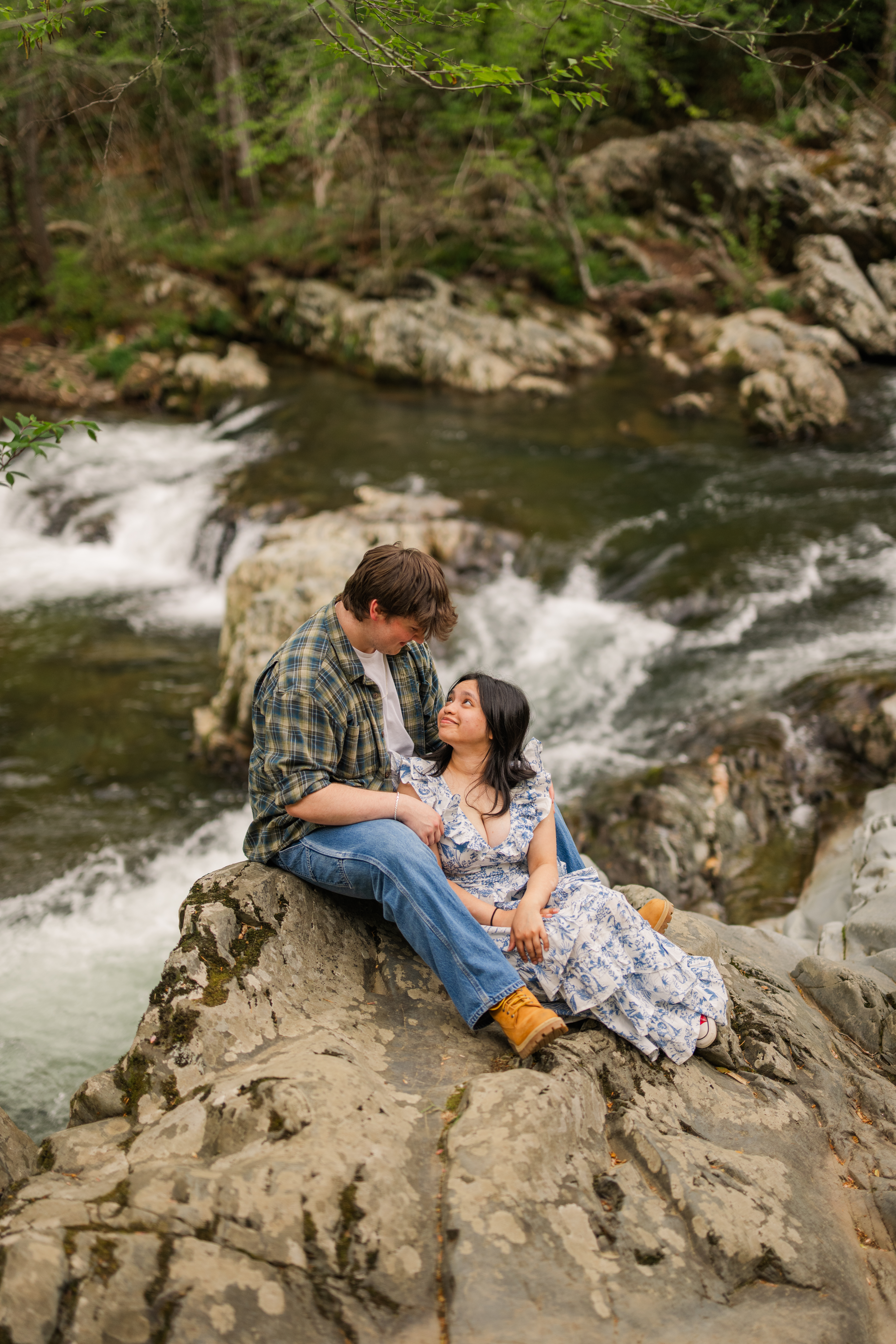 Engaged couple snuggled on a large rock above river rapids during engagement session in Great Smoky Mountains National Park at Greenbrier, Tennessee