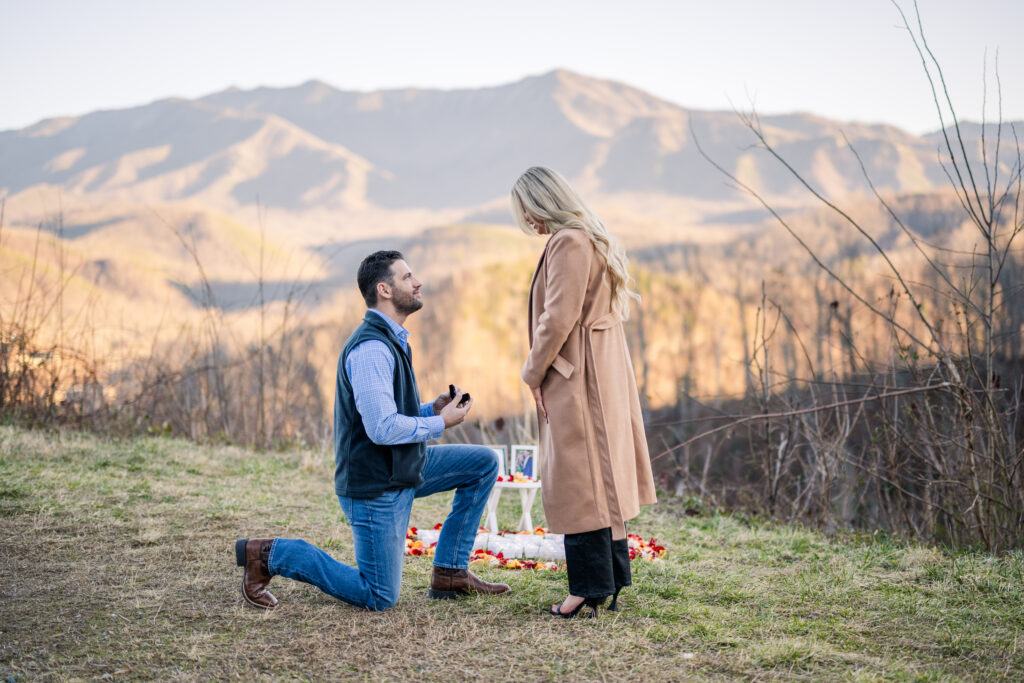 A proposal between a man and woman with the great smoky mountains in the background surrounded by rose petals 