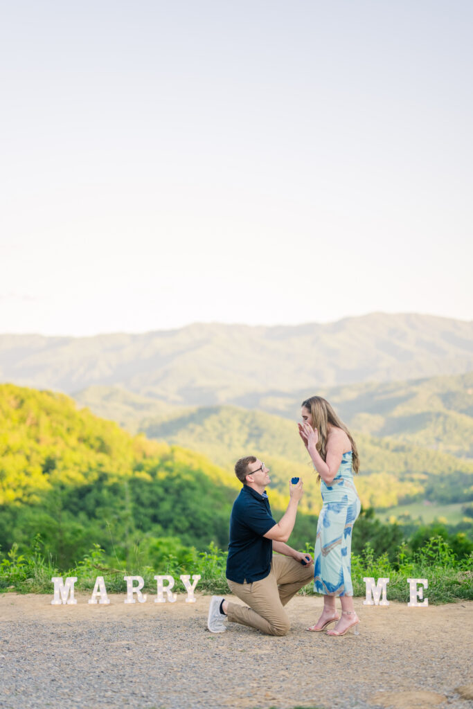 a man proposing to a woman in pigeon forge tn with the mountain in the background and a sign that says marry me