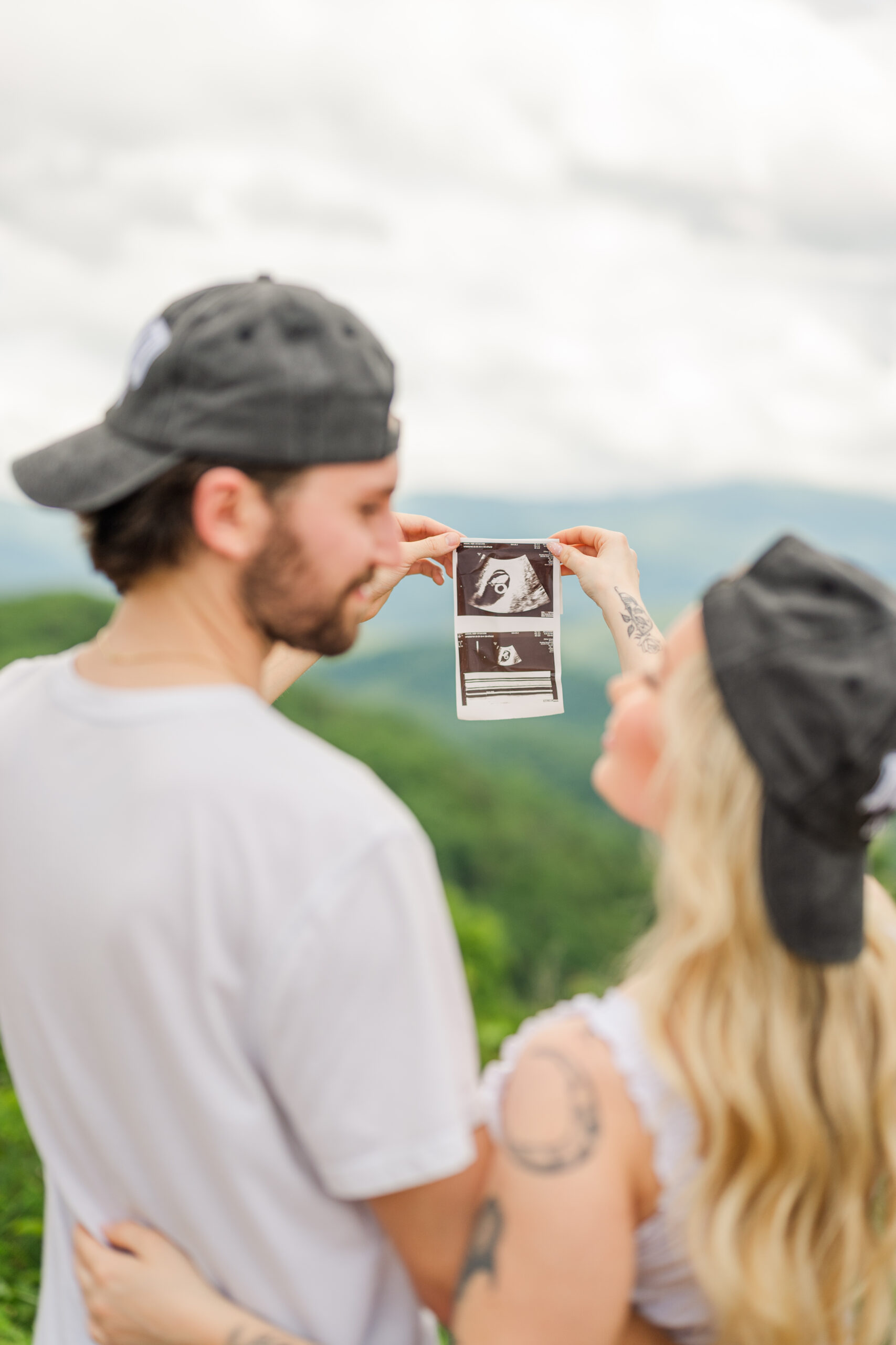 couple celebrating pregnancy on vacation in Gatlinburg with the Smoky Mountains in the background